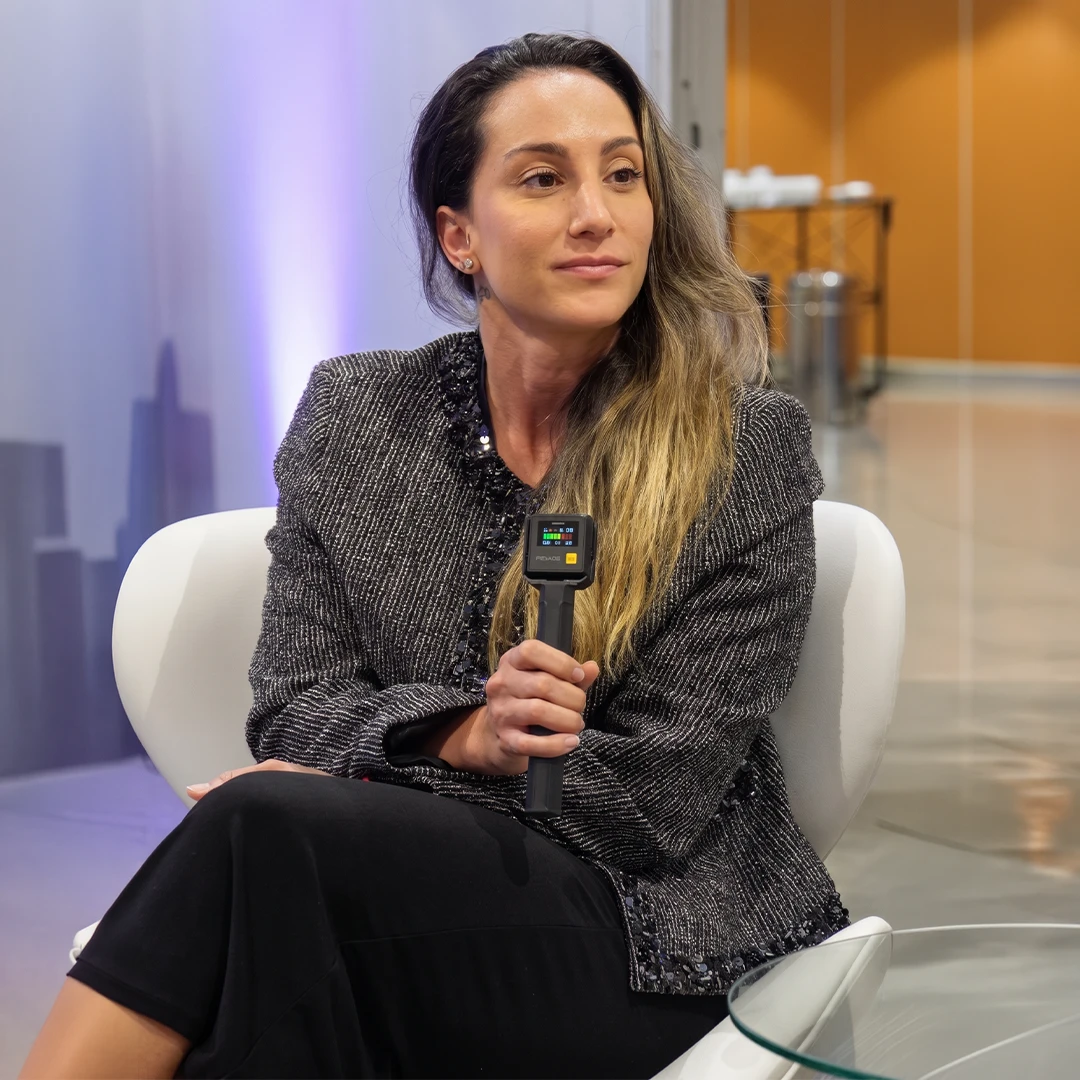 Dra. Thaís Fonseca palestrando em evento, com terno tweed e microfone na mão